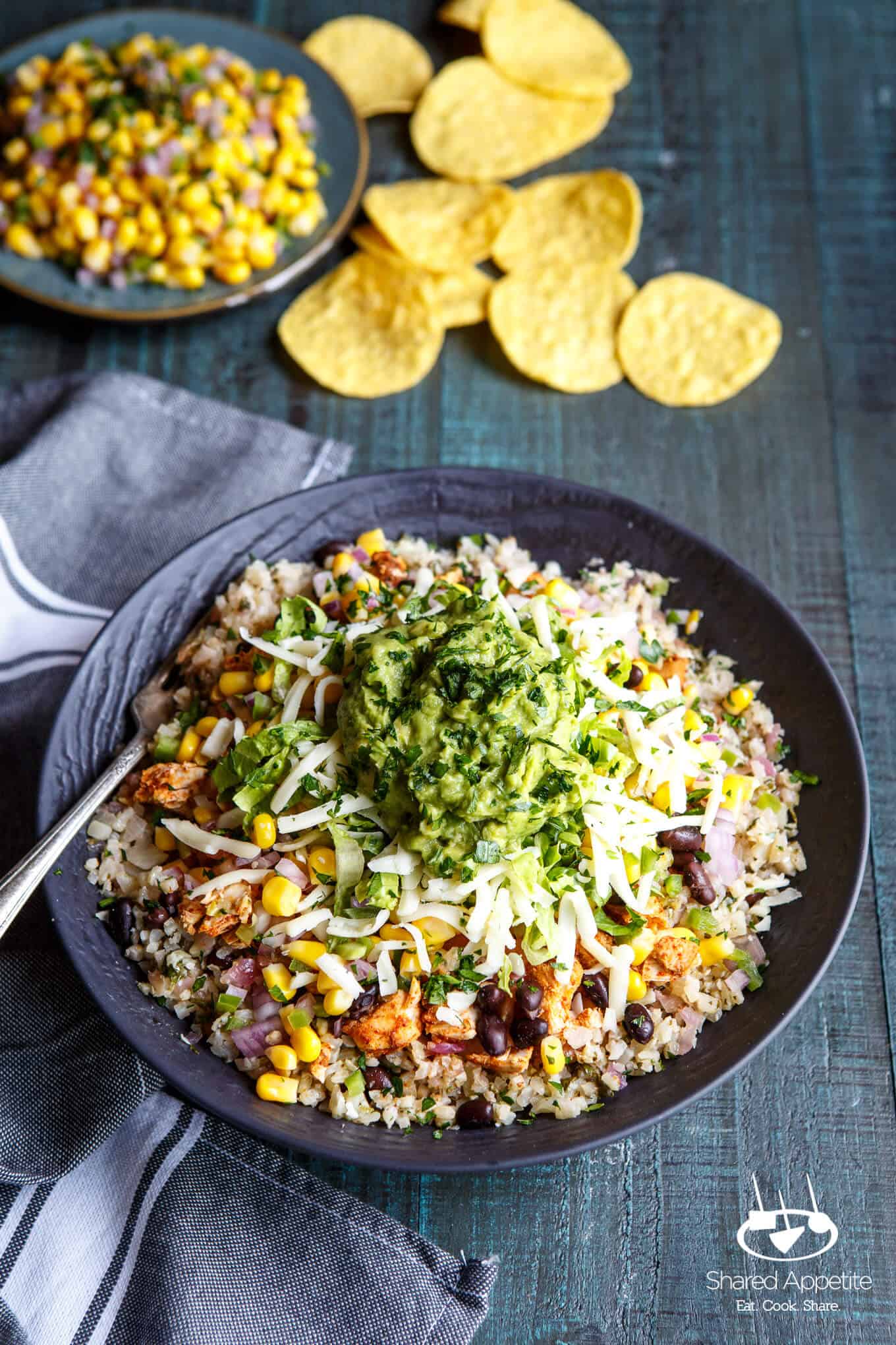 Healthy Cauliflower Rice Burrito Bowls with tortilla chips and corn salsa in the background | sharedappetite.com